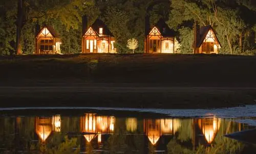 Quatre chalets éclairés de nuit, se reflétant dans l'eau