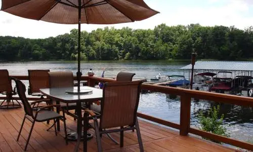 Une terrasse avec des chaises et un parasol donnant sur un lac avec des bateaux amarrés à proximité.