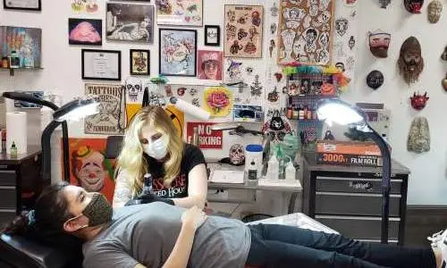 Une femme s'allonge sur une chaise et se fait tatouer par un tatoueur.