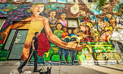 Un homme promenant trois chiens devant une peinture murale colorée.