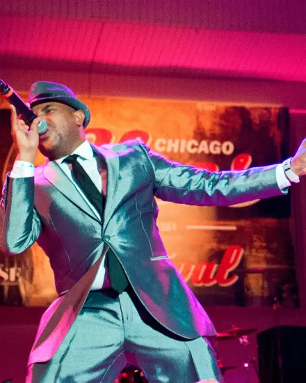 Un chanteur de blues vêtu d'un élégant costume aux tons métalliques chantant à plein poumon sur scène.