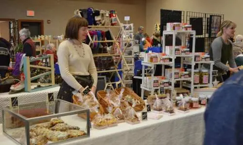 Une femme se tient derrière des produits de boulangerie sur une table.