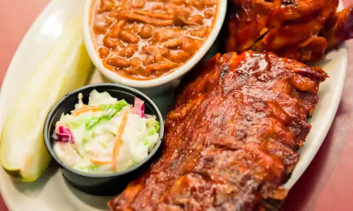 Une assiette de plats bbq comprenant des côtes, de la salade et des haricots.