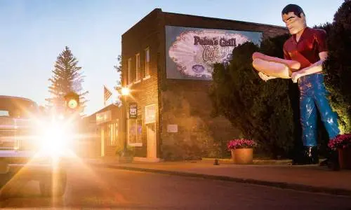 Coucher de soleil derrière une voiture avec une statue géante d'un homme tenant un hot-dog