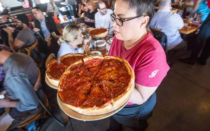Un serveur de Giordano's transportant deux pizzas dans un restaurant très fréquenté.
