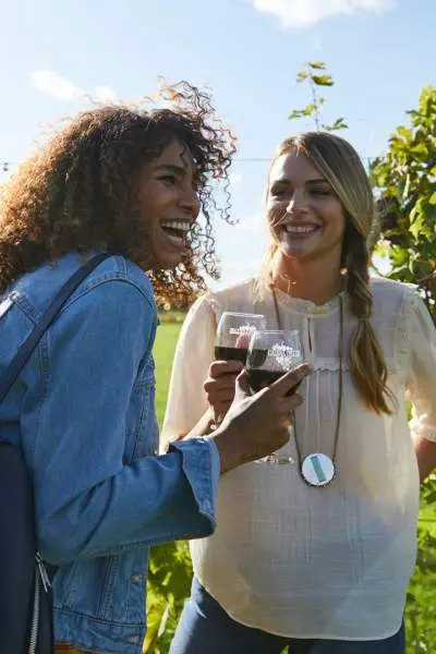 Deux filles rient en dégustant du vin rouge dans un vignoble