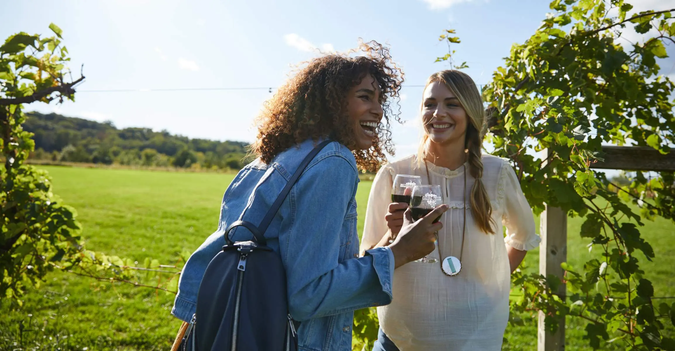 Deux filles rient en dégustant du vin rouge dans un vignoble