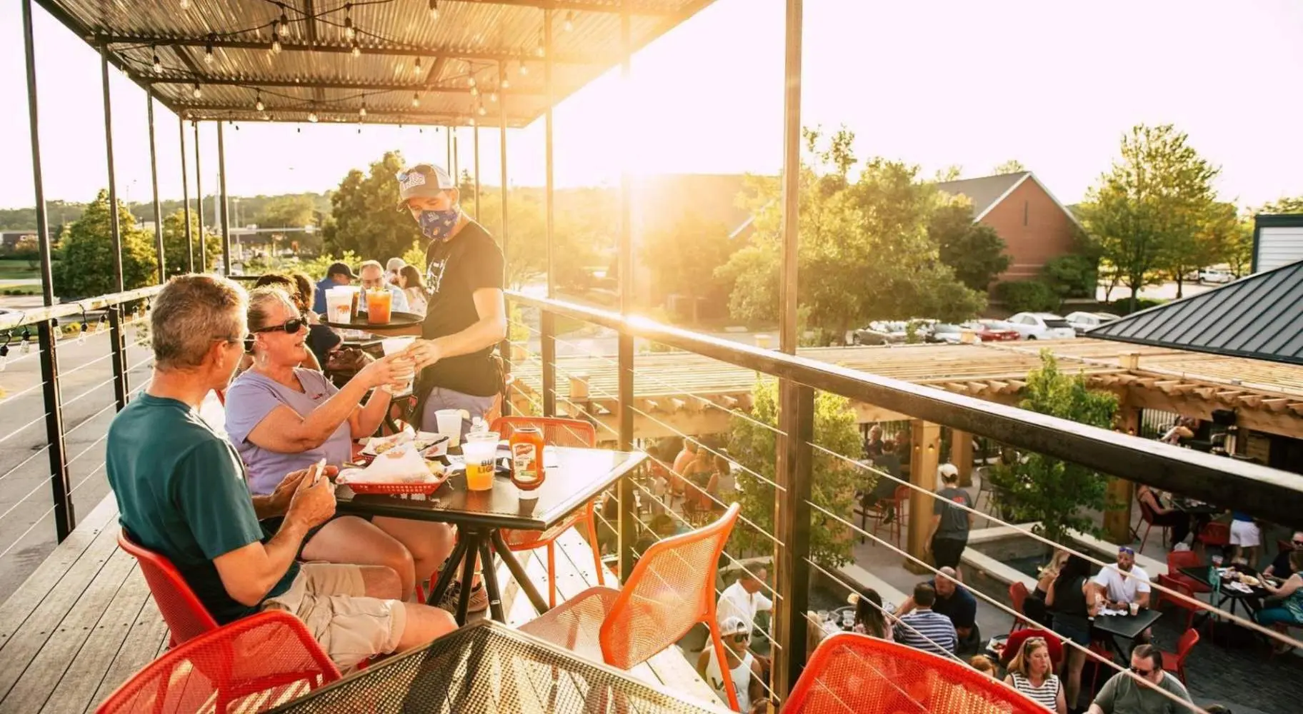 Personnes se faisant servir de la nourriture sur la mezzanine ensoleillée d'un restaurant en plein air.