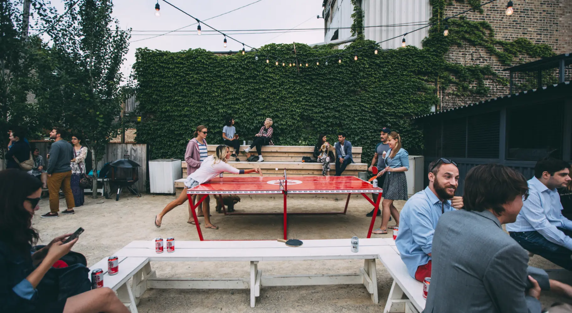 Des clients boivent des bières et jouent au tennis de table en plein air.