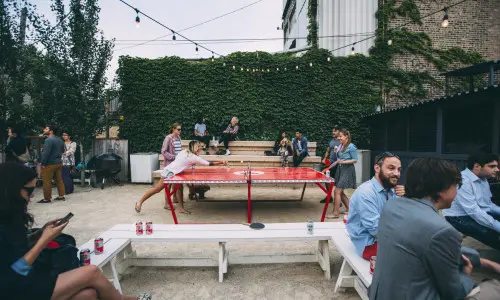 Des clients boivent des bières et jouent au tennis de table en plein air.