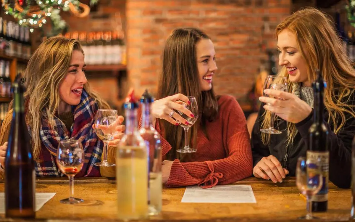 Trois femmes assises à une table dégustant un verre de vin à l'intérieur d'une cave à vin