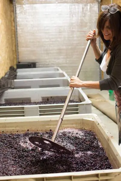 Une femme mélange les raisins dans un grand récipient pour faire du vin.