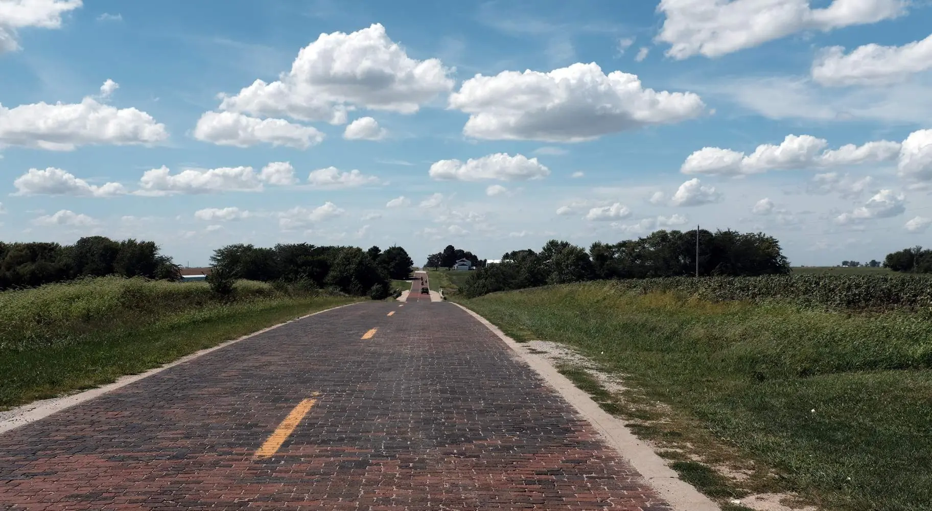 Une route en briques à l'ancienne entre des champs ruraux verdoyants