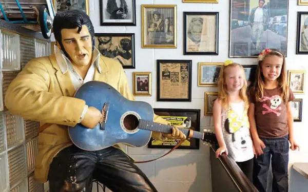 Deux jeunes se font photographier à côté d'une statue d'Elvis Presley tenant une guitare.