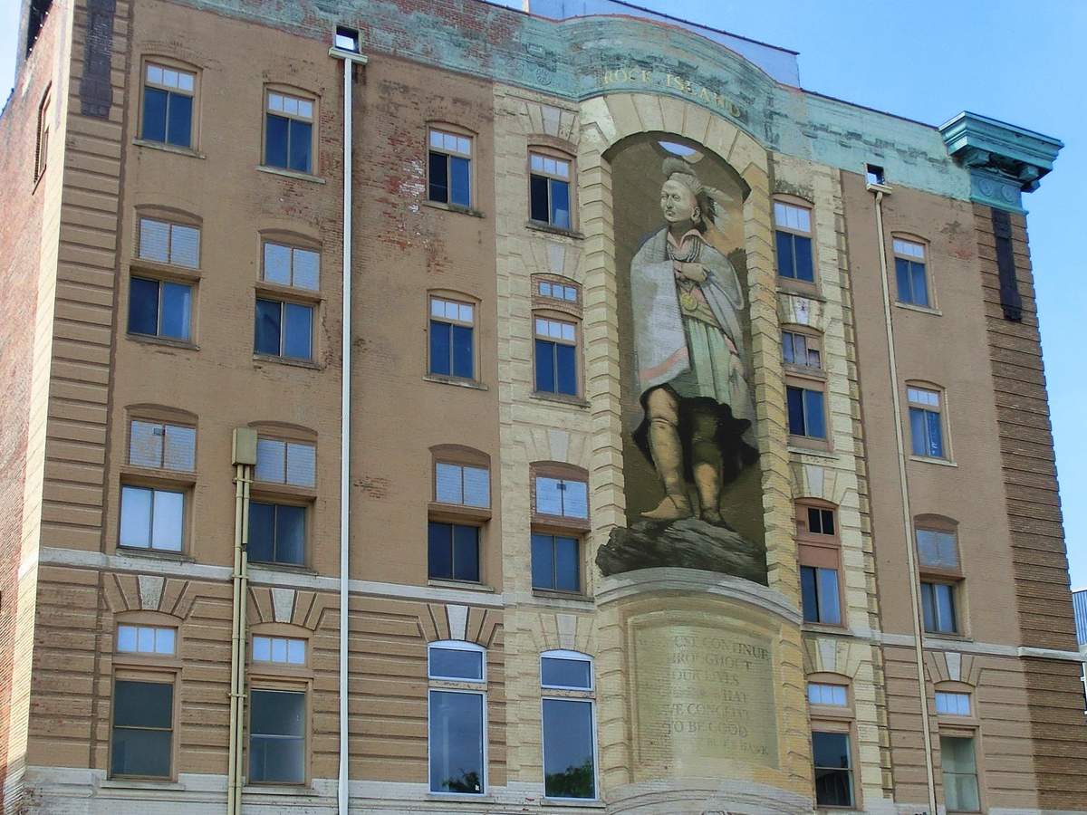 Une grande peinture murale de Blackhawk, haute de trois étages, sur la façade d'un bâtiment en briques.