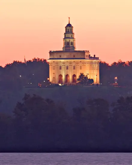Un temple avec des lumières allumées derrière des arbres et une rivière