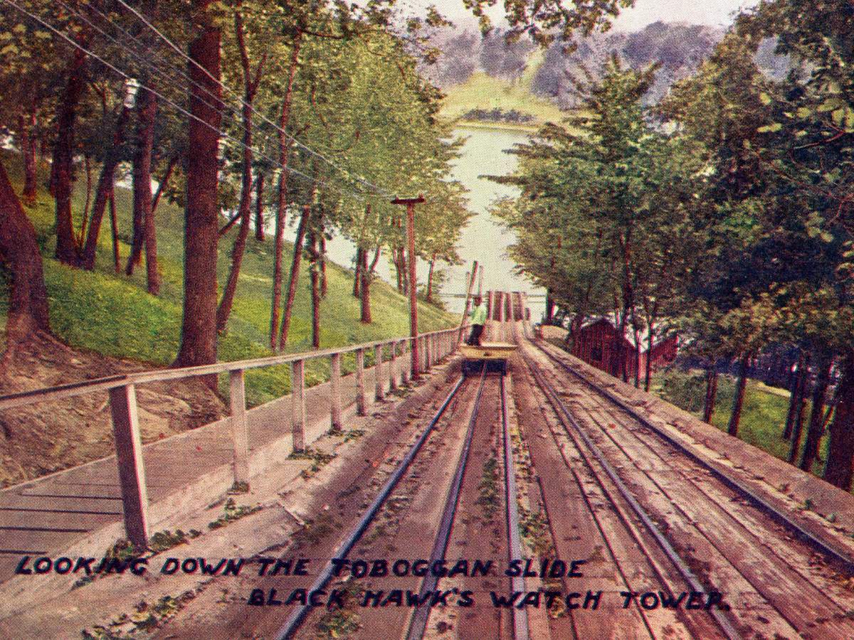 Carte postale ancienne d'un parc d'attractions sur rails, au milieu des arbres