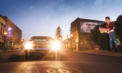 Une voiture de collection avec ses phares allumés, à côté de la statue géante de Paul Bunyon à Atlanta