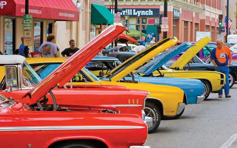 Des voitures anciennes aux couleurs vives, capot ouvert, sont alignées dans une rue du centre-ville à l'occasion d'un rassemblement automobile sur la Route 66.