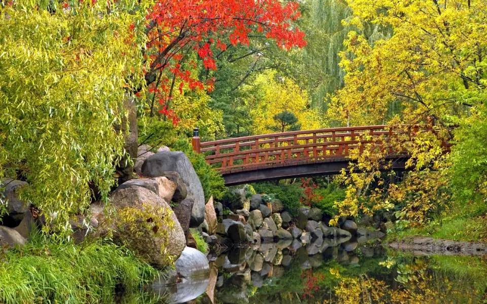 Un pont traverse un étang entouré de feuillages d'automne.