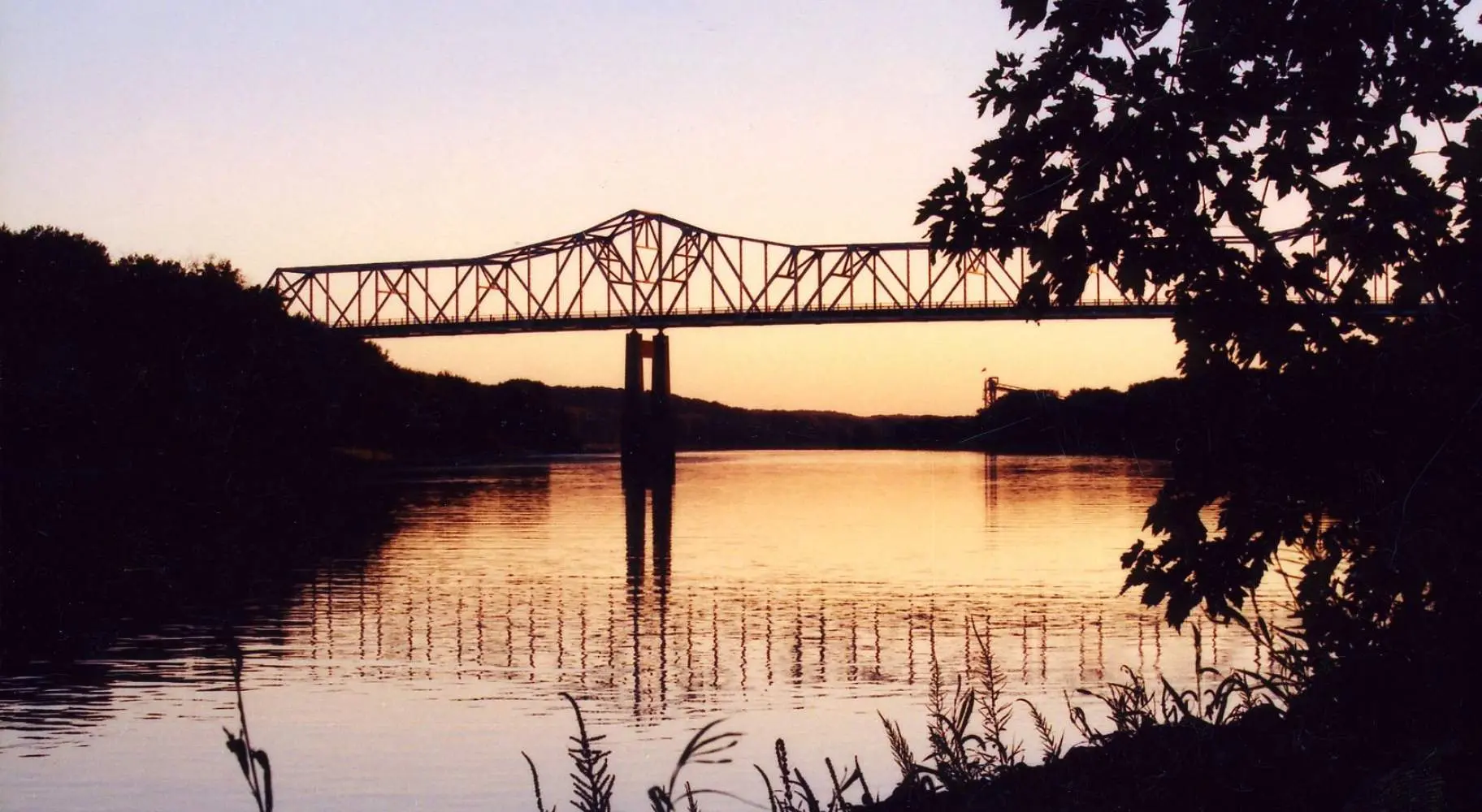 Pont enjambant une rivière au coucher du soleil, vu de la rive