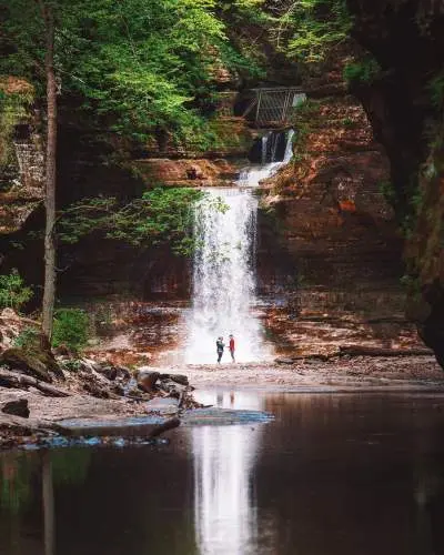 Deux personnes se tenant devant une cascade, à côté d'un étang serein.