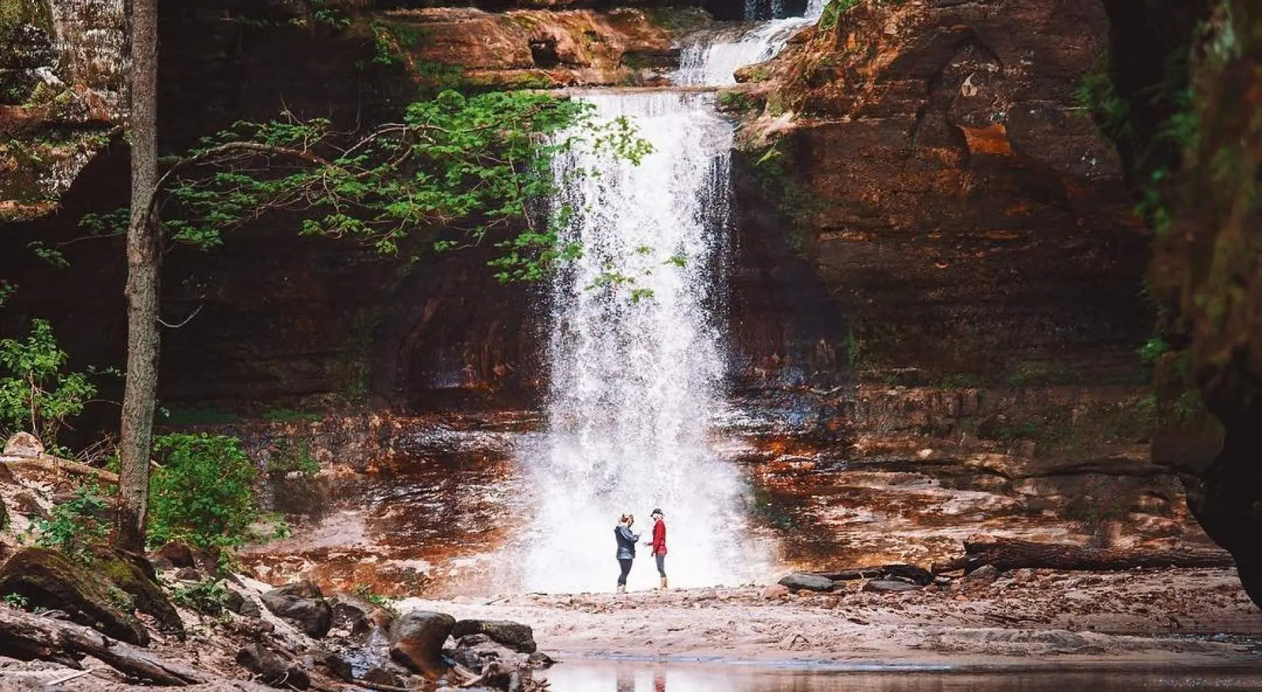 Deux personnes se tenant devant une cascade, à côté d'un étang serein.