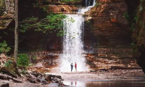 Deux personnes se tenant devant une cascade, à côté d'un étang serein.
