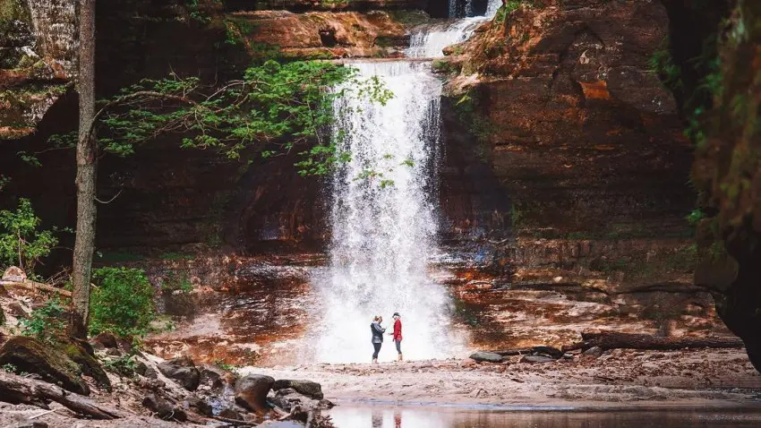Deux personnes se tenant devant une cascade, à côté d'un étang serein.