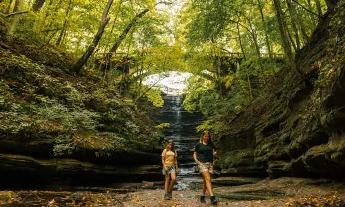 Deux jeunes filles marchent devant une cascade dans le parc d'État de Matthiessen.