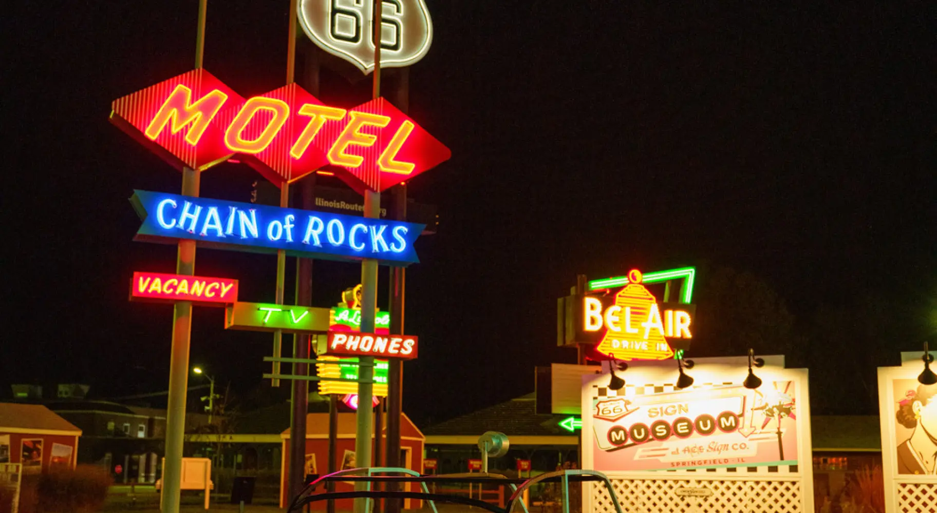 Des enseignes vintage au néon de motels de la Route 66 et une voiture à pédales classique, illuminées la nuit.
