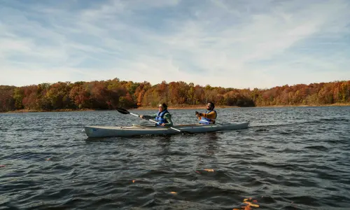 Deux kayakistes sur un lac bordé de feuillages d'automne.