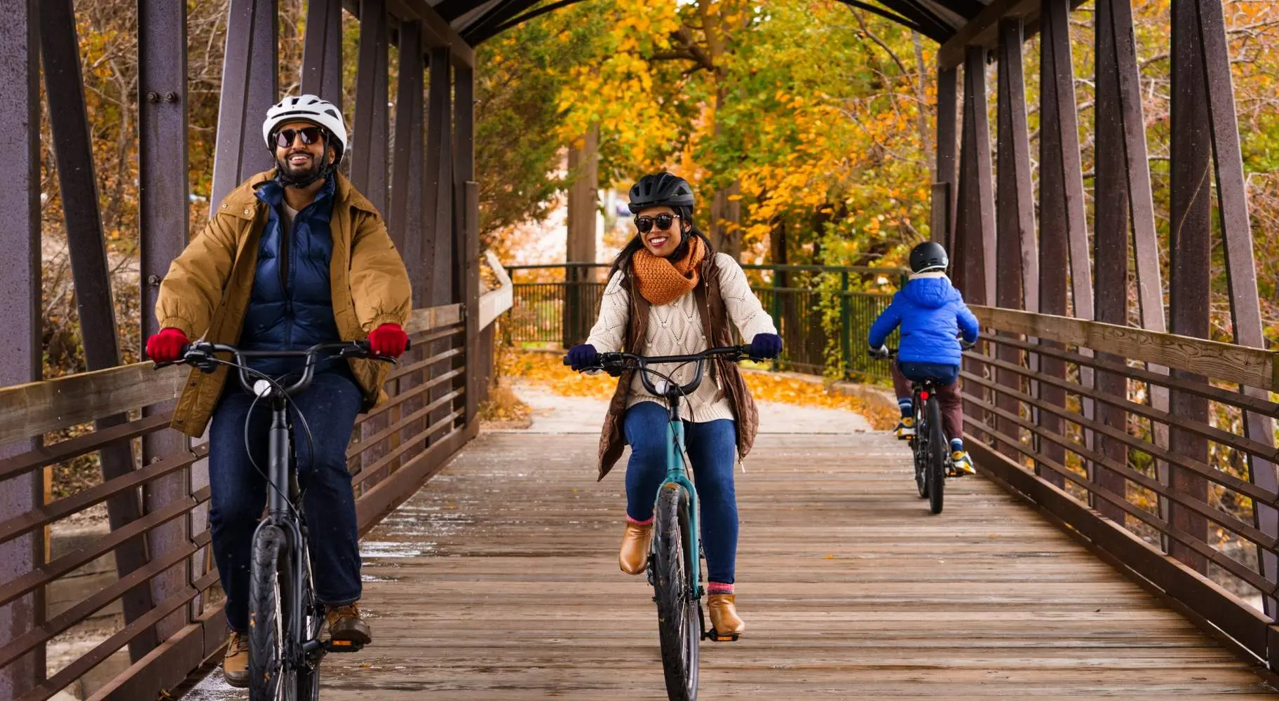 Un couple à vélo sur un vieux pont couvert de bois, avec le feuillage d'automne derrière eux