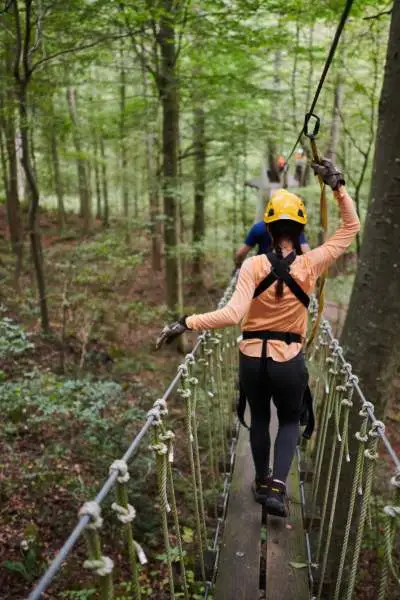 Des personnes sur un pont traversant les forêts avec des harnais et des casques de sécurité à Canopy Tours.