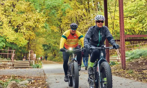 Deux cyclistes roulant sur un sentier boisé sous un vieux pont de bois