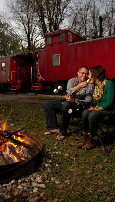 Couple grillant des marshmallows sur le feu de joie avec un train derrière eux.