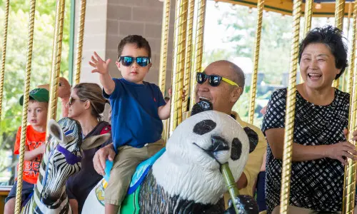 Un enfant en bas âge et ses grands-parents sur le manège du zoo de Brookfield.