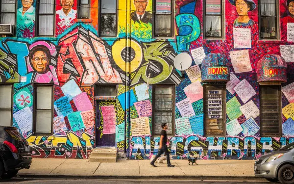 Une personne avec un chien marchant devant une peinture murale représentant le patrimoine mexicain