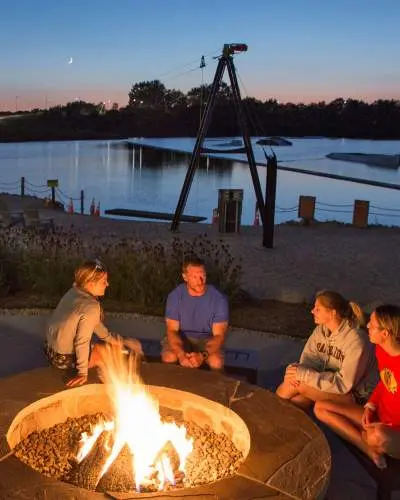 Quatre personnes assises autour d'un feu sur une plage au bord d'un lac au crépuscule