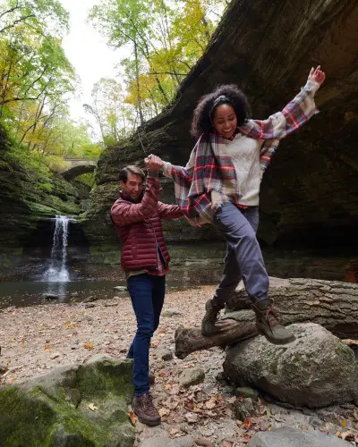 Deux personnes grimpant sur des rochers devant une chute d'eau.