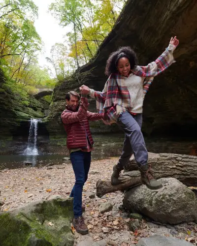 Two people climbing on rocks in front of a rock waterfall