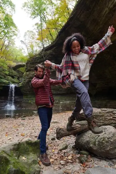 Deux personnes grimpant sur des rochers devant une chute d'eau.