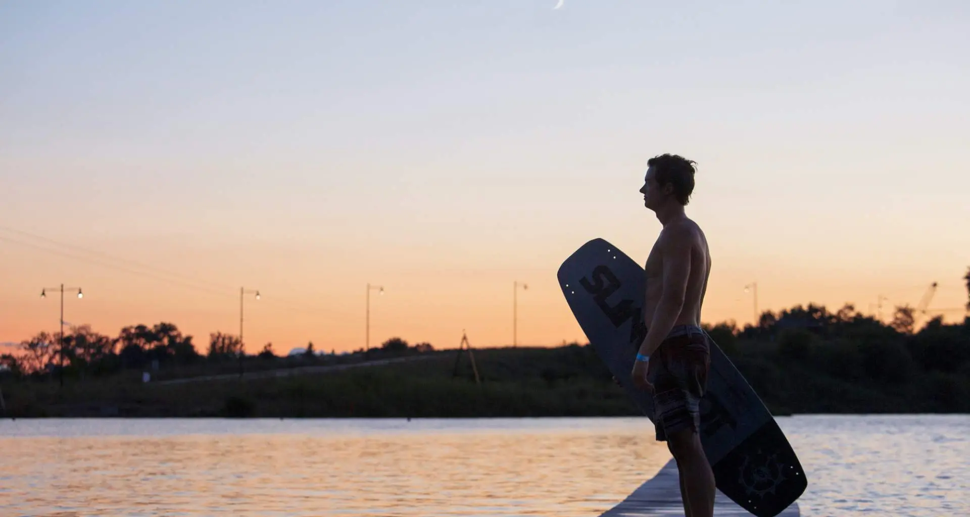 Un wakeboarder se tient à côté du Quarry Cable Park à la tombée de la nuit.