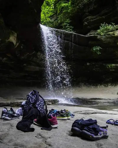 Une chute d'eau depuis un rocher, avec les sacs et les chaussures des gens qui gisent sur le rocher en dessous.