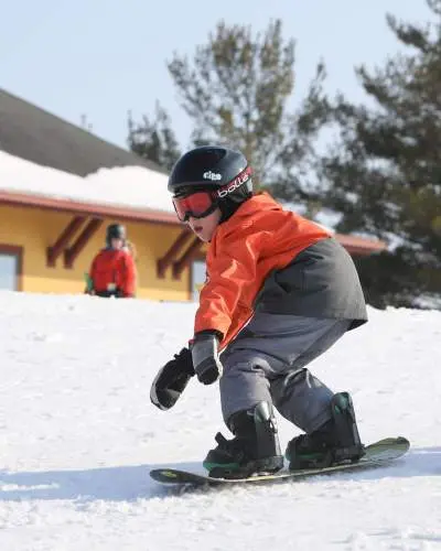 Un petit enfant faisant du snowboard sur la neige, portant un casque, des lunettes et des vêtements de ski chauds.