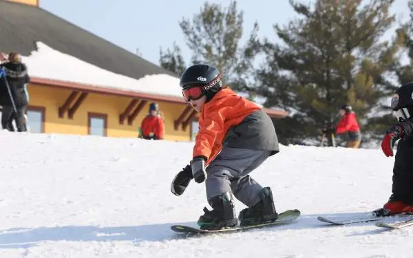 Un petit enfant faisant du snowboard sur la neige, portant un casque, des lunettes et des vêtements de ski chauds.