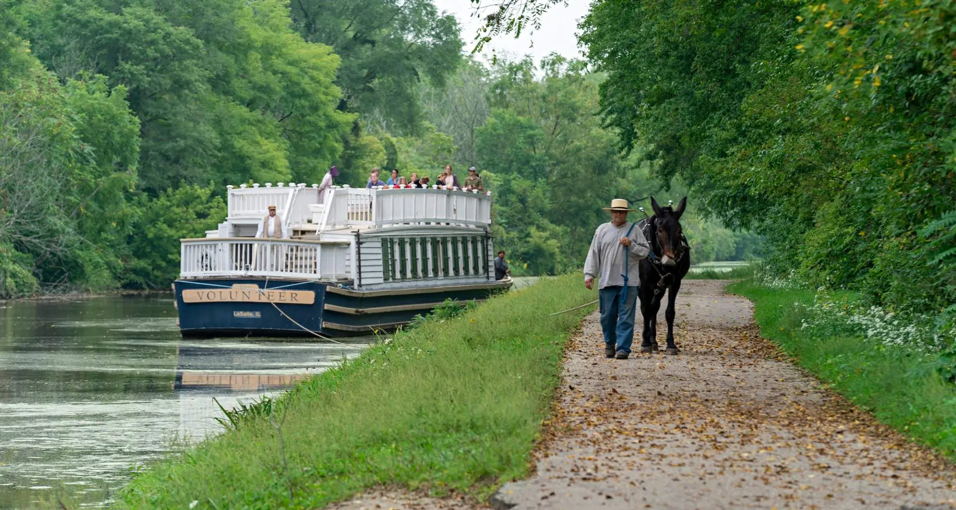 Un bateau descendant la rivière et un homme promenant une mule sur un sentier.