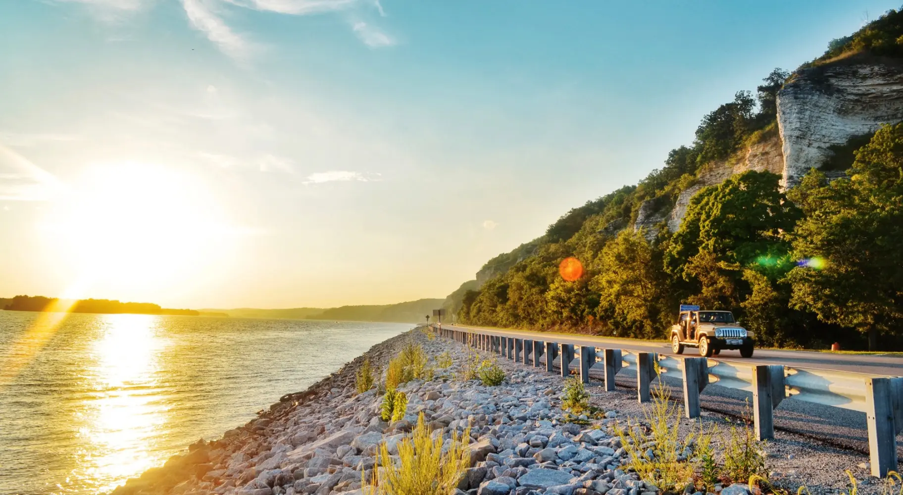 Le soleil se lève sur l'eau et une voiture roule sur la route d'à côté