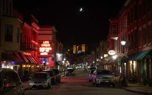 Rue principale d'une petite ville la nuit, avec des voitures de chaque côté de la route et une enseigne lumineuse au néon indiquant "Log Cabin" (cabane en rondins)