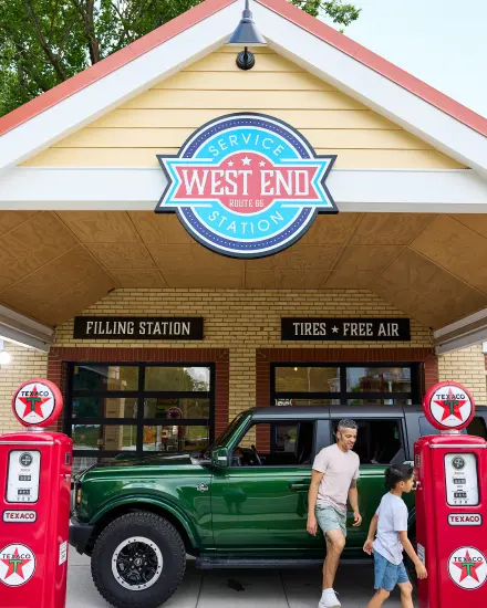 Un père et son fils passent devant un SUV vert et des pompes à essence d'époque à la station-service West End, sur la Route 66.